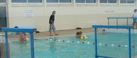 A swimming pool with a lifeguard tower, a sign indicating no diving, and a fenced area with chairs.