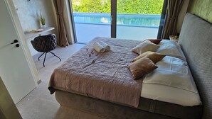 A bedroom with a large bed, a small table, and a view of a pool outside. - Stylish villa *****, heated pool (Rakalj)