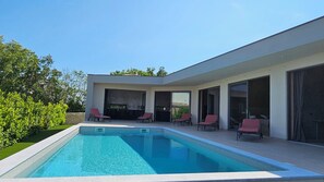 Ein modernes Haus mit Swimmingpool, roten Liegestühlen und großen Glasfenstern.