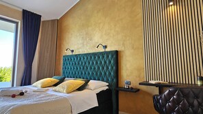 Ein Hotelzimmer mit einem großen Bett, einem Nachttisch, einem Sessel und Blick auf Grünfläche.