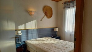 A bedroom with a bed, two bedside lamps, a wall-mounted fan, and a window with curtains. - .Maison Quiet, sunny position good in 10 'from the beach residence (Fleury)