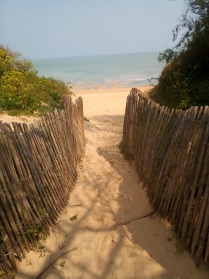 Ein sandiger Pfad führt zu einem Strand, begleitet von einem Holzzaun auf beiden Seiten.