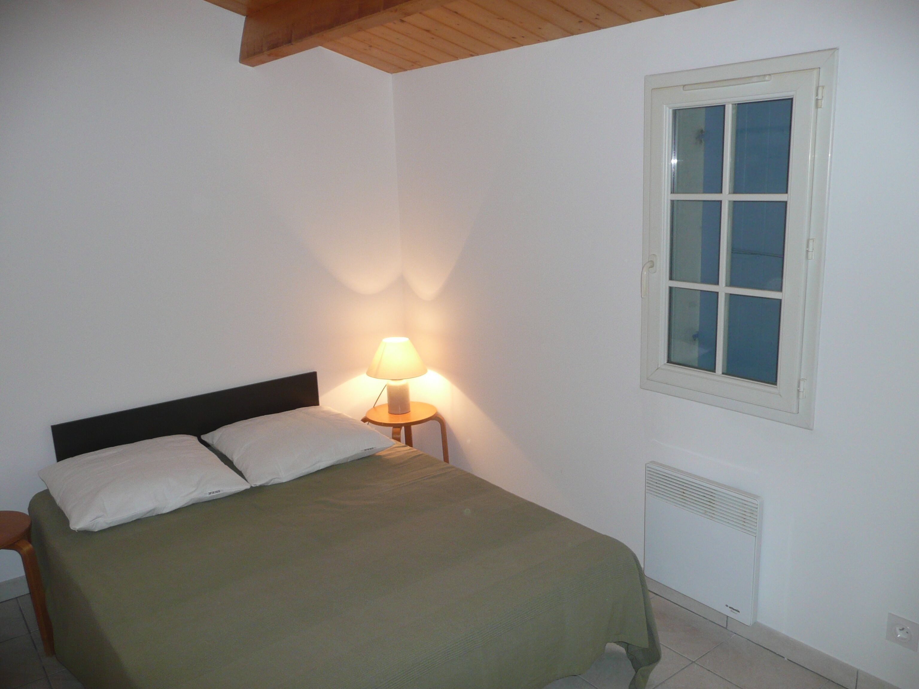 A simple bedroom with a bed, a nightstand, a lamp, and a window.