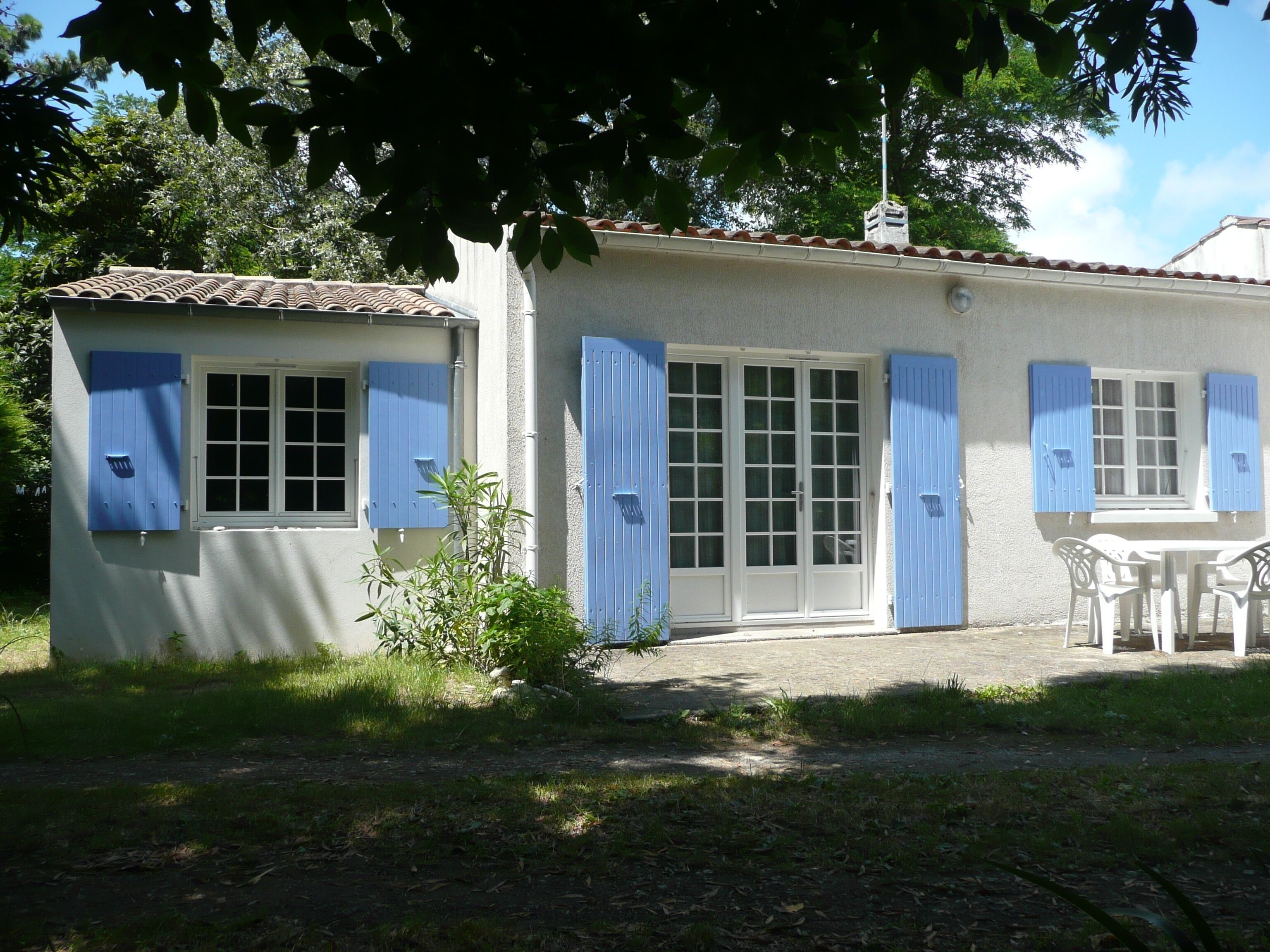 Una casa con techo de tejas, puerta principal y un pequeño patio con mesa y sillas.