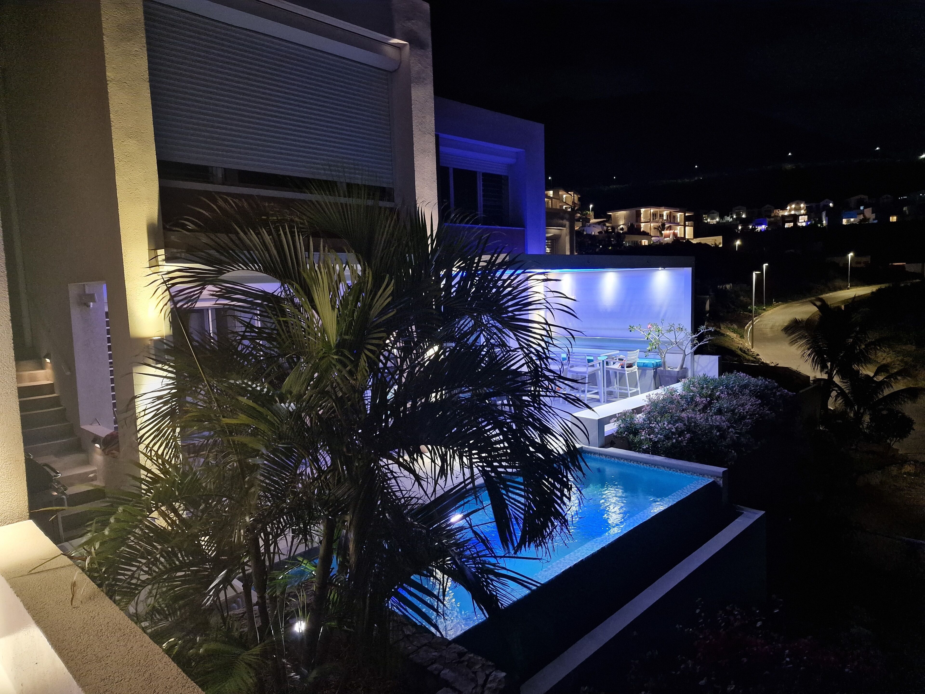 Un edificio moderno con piscina, palmeras y un área exterior bien iluminada.