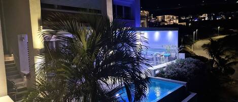 Un edificio moderno con piscina, palmeras y un área exterior bien iluminada.