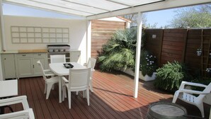 A covered patio with a wooden deck, white furniture, a grill, and potted plants. - Charming house near the beach, detached, not overlooked, WIFI. (Arvert)