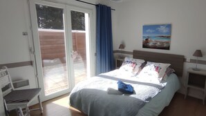 A bedroom with a bed, a nightstand, a lamp, a painting, and a sliding glass door leading to an outdoor area. - Charming house near the beach, detached, not overlooked, WIFI. (Arvert)
