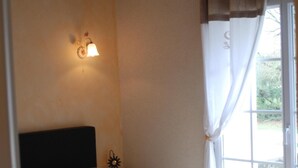 A bedroom with a bed, a nightstand, a wall-mounted light, and a window with curtains.