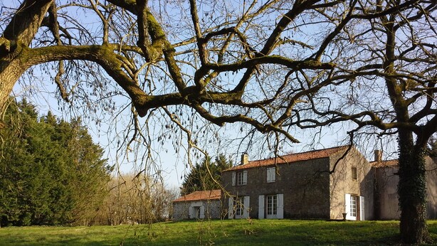 A rustic stone building with a tiled roof, surrounded by a grassy field and trees.