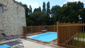 A swimming pool with a wooden fence, lounge chairs, and a stone building in the background.