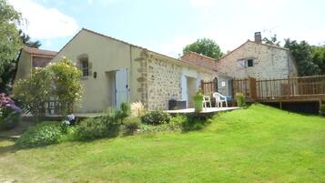 Une maison en pierre à deux étages, dotée d’un petit jardin et d’une terrasse en bois.