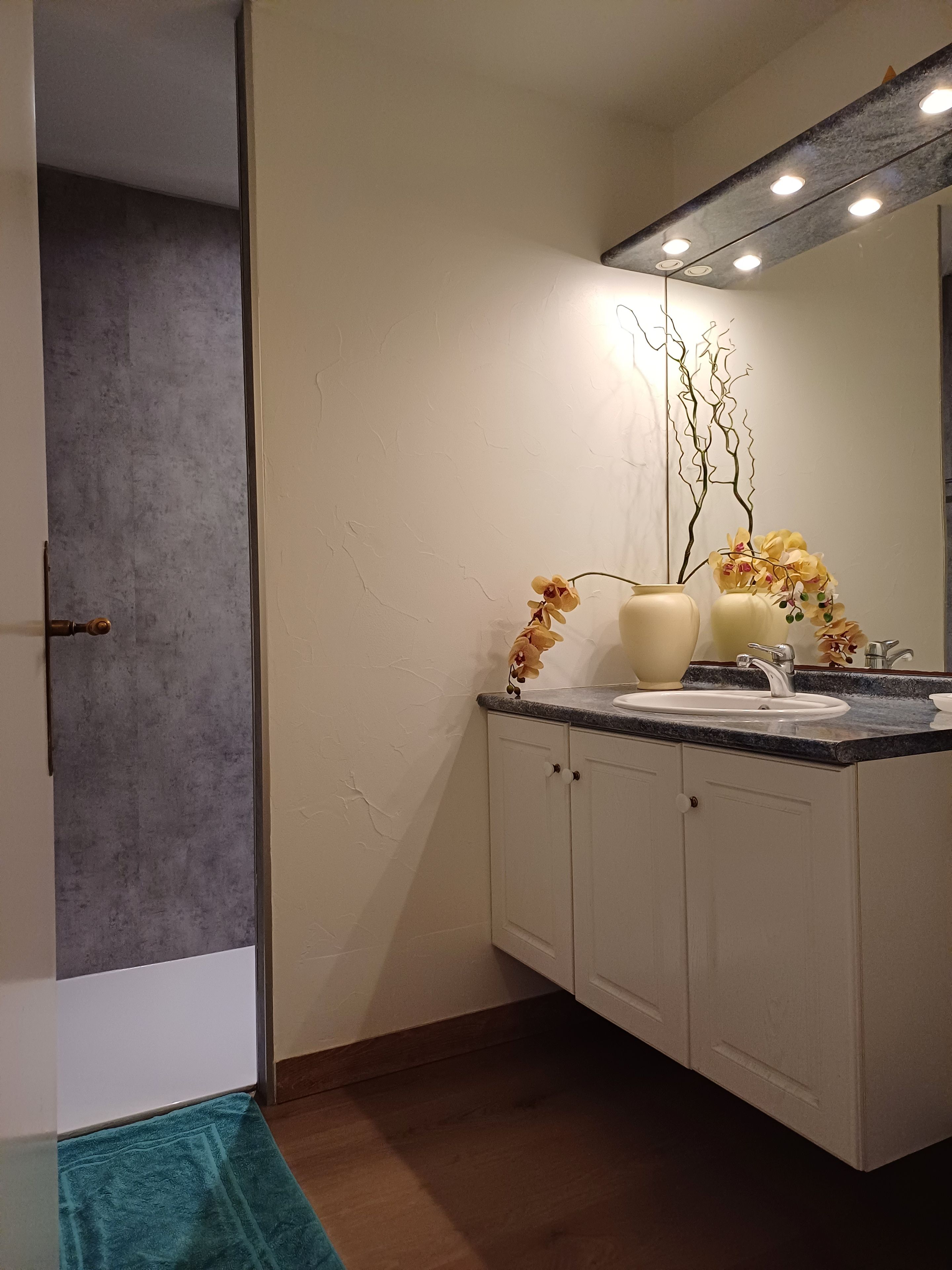A bathroom with a white vanity, a sink, and a mirror above it. There are two vases with flowers on the counter.