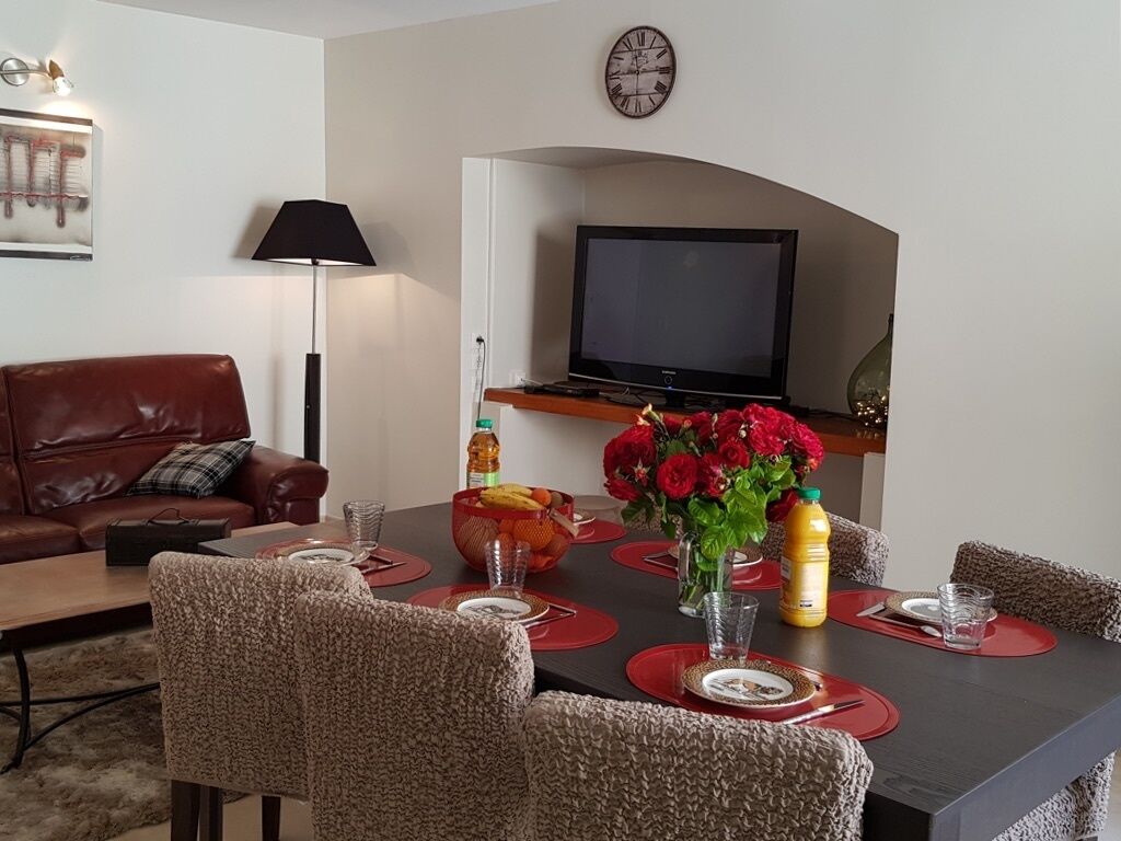 A dining area with a table set for six, surrounded by six chairs. A television is mounted on the wall above the table.