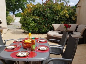 Un espace extérieur aménagé pour prendre les repas, avec une table dressée pour quatre personnes, entourée de chaises.
