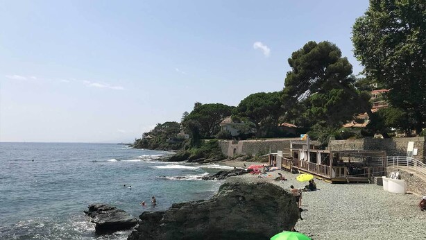 Una playa rocosa con una estructura de madera y sombrillas, con vista al mar.