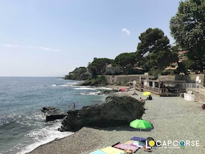 A rocky beach with a wooden structure and umbrellas, overlooking the sea.