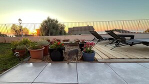 Una terraza en la azotea con plantas en macetas, un gato y dos tumbonas.