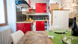 A modern kitchen with red cabinets, a wooden countertop, and a dining area with a green tablecloth. - Superb apartment (3pers) air-conditioned, quiet, ideal location in town center (Nîmes)