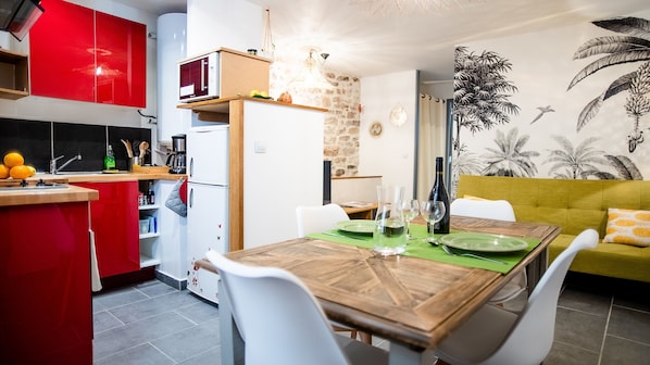 A compact kitchen with red cabinets, a white refrigerator, and a dining area with a wooden table set for two.