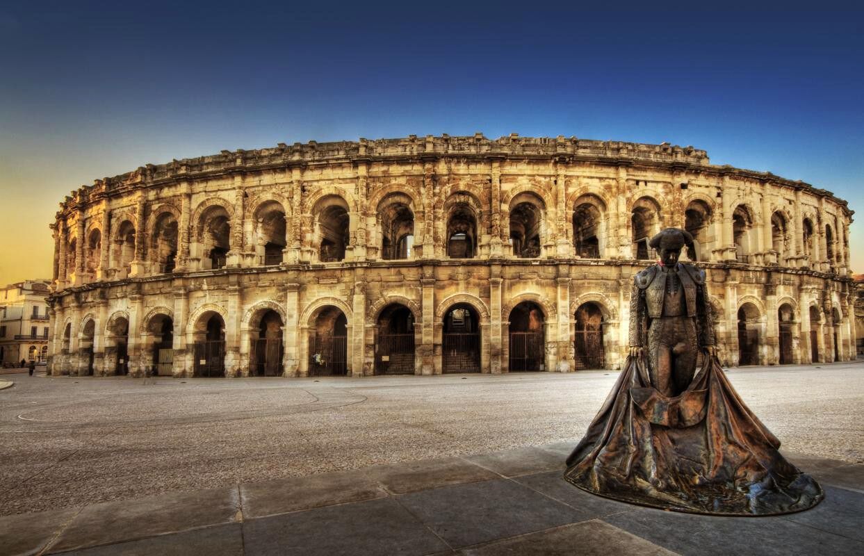 A historic building with a large open courtyard and a statue in the foreground.