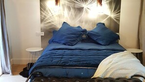 A modern bedroom with a bed, a small white side table, and a headboard with light fixtures. - Grand cru house (Chardonnay)