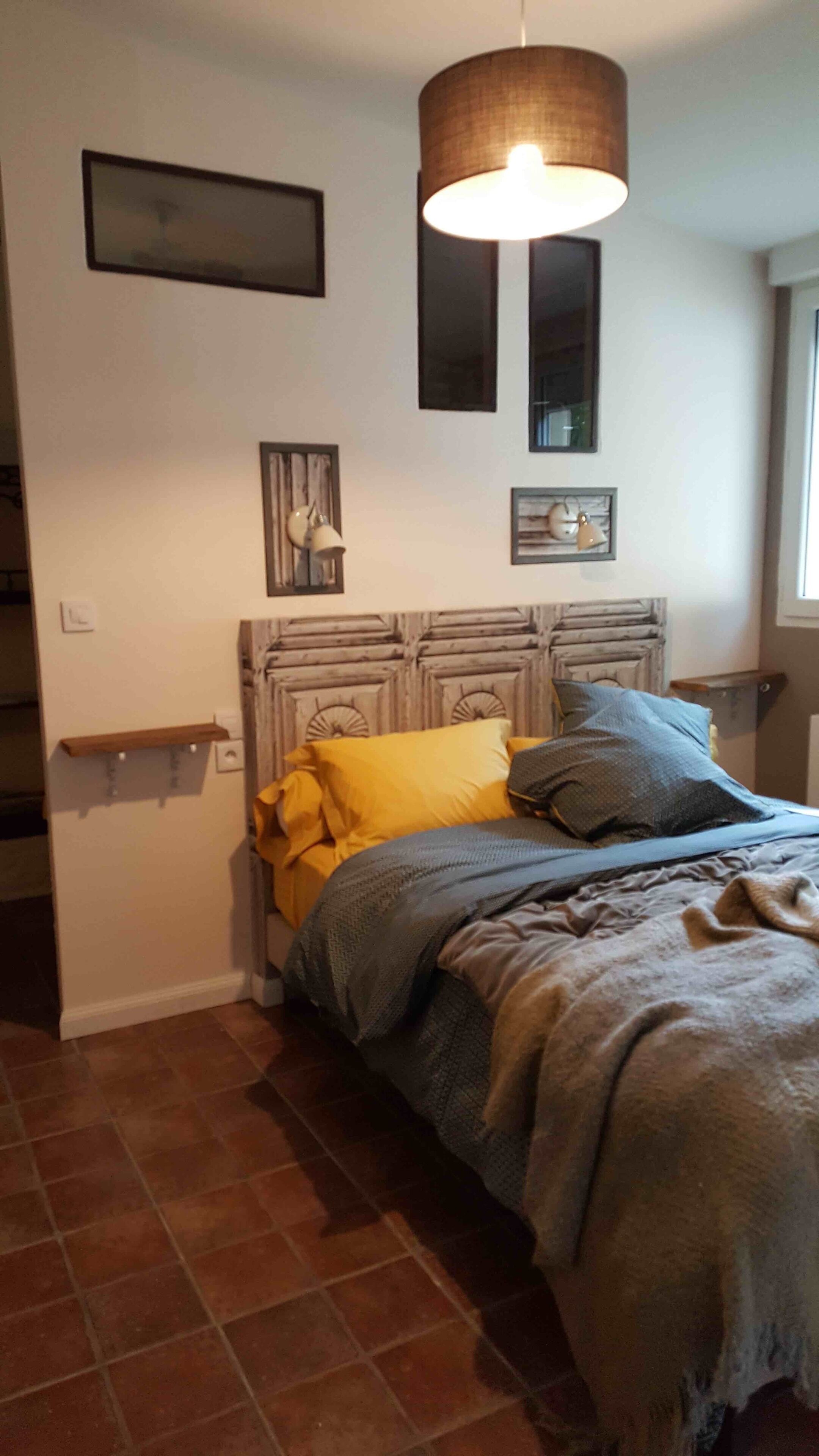 Une chambre à coucher avec un lit, une tête de lit, une lampe suspendue et une fenêtre.
