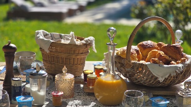 A table with a basket of bread, a bottle of honey, and various jars of preserves. - Grand cru house (Chardonnay)