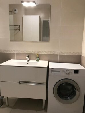 A compact bathroom with a white sink, a mirror above it, and a front-loading washing machine. - T3 Golden Triangle : Annecy Green *** (ANNECY)