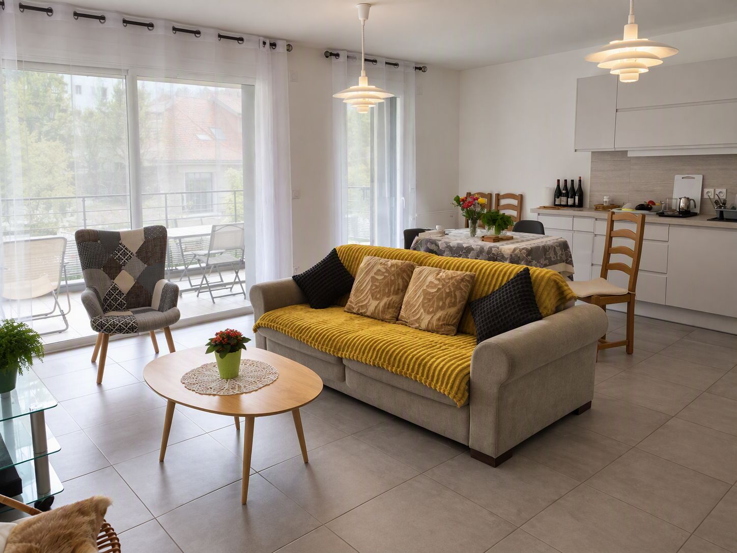 A modern living room with a sofa, armchairs, and a dining table. There is a kitchen area with cabinets and a dining table.