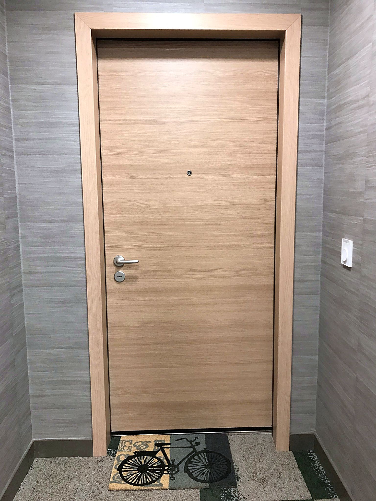 A wooden door with a handle and a keyhole, set in a hallway with grey walls and a carpeted floor.