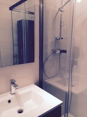 A modern bathroom with a glass-enclosed shower, a white sink, and a mirror above the sink.