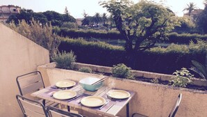 Une terrasse extérieure avec une table dressée pour quatre personnes, entourée de chaises, donnant sur un jardin aménagé.