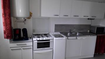 Une cuisine avec des meubles blancs, une cuisinière, un four, un four à micro-ondes et un évier.