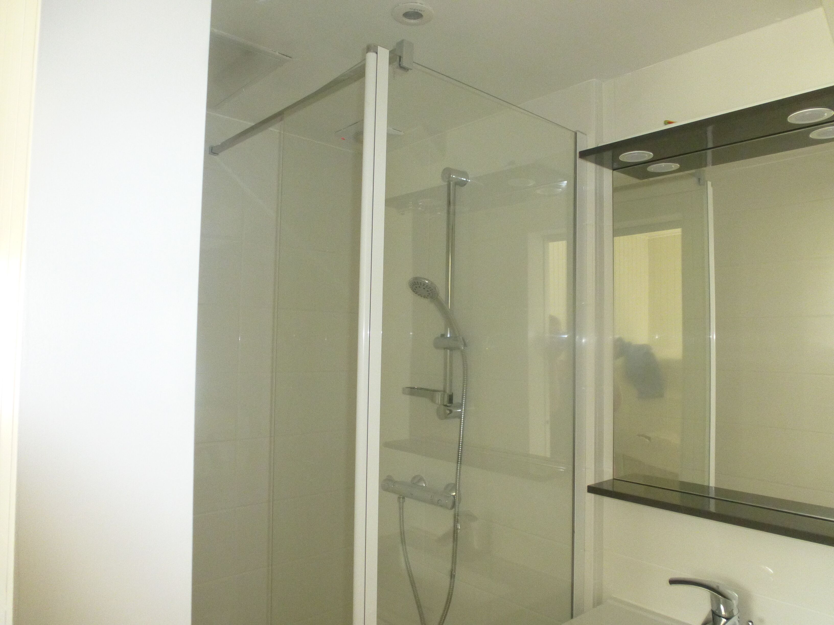 A modern bathroom with a glass-enclosed shower, a mirror, and a sink.