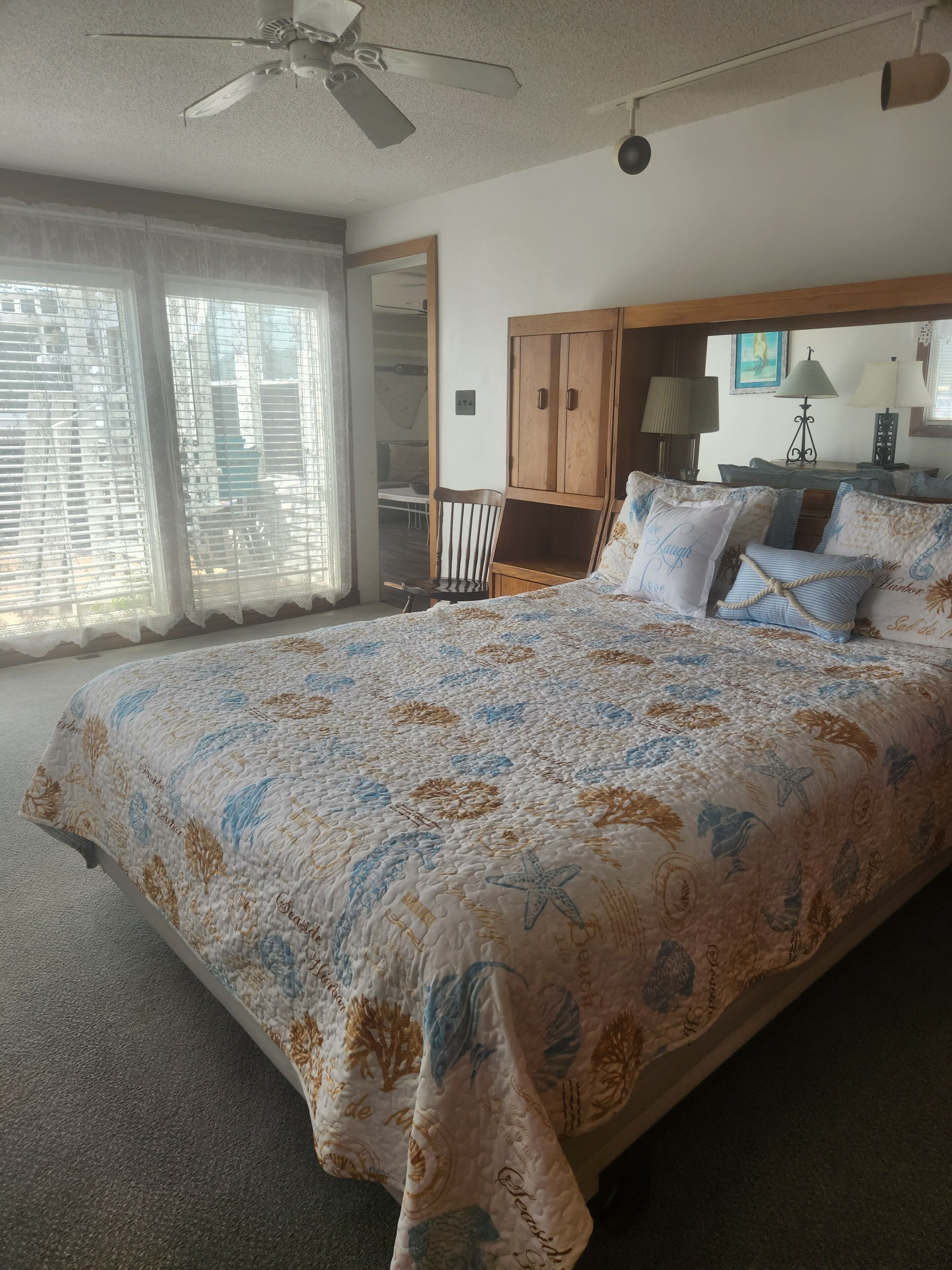 A bedroom with a large bed, a wooden wardrobe, a ceiling fan, and a window with blinds.