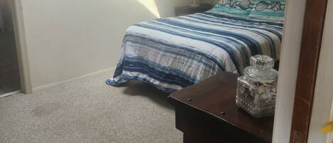 A bedroom with a bed, a nightstand, a lamp, and a framed picture on the wall.