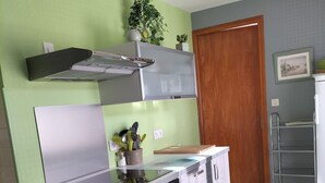 A compact kitchen with a built-in oven, a microwave, and a stove. There is a wooden door and a small shelf with plants. - Guillestre ground-floor rental for 2 to 4 people, beautiful south-facing view. (Guillestre)
