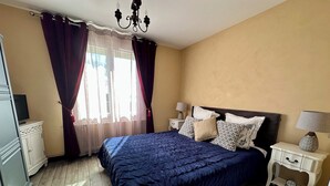 A bedroom with a large bed, a nightstand, a lamp, a dresser, and a window with curtains. - THE ANNEX holiday home in the heart of the vineyard (Verdigny)
