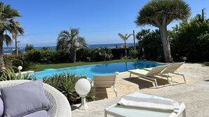 A pool area with lounge chairs and a view of the sea.
