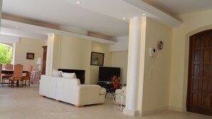 A spacious living area with a sofa, television, and a dining table with chairs.