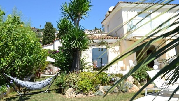 A garden with a hammock, palm trees, and a building with a tiled roof.