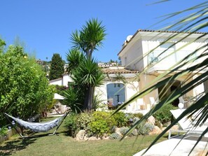 Un jardin avec un hamac, des palmiers et un bâtiment doté d’un toit en tuiles.