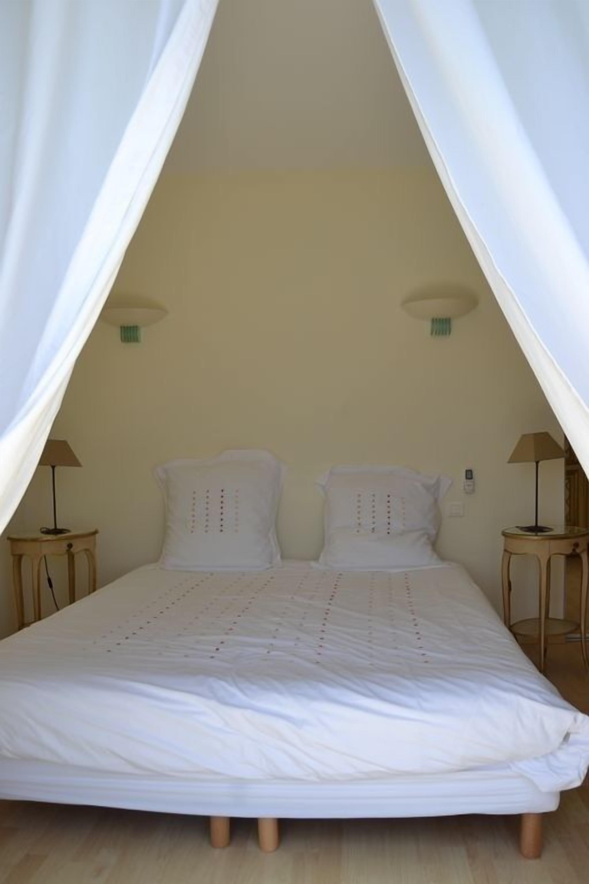 A single bed with a canopy, two bedside tables, and a wall-mounted lamp.