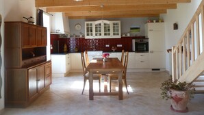 A spacious kitchen with wooden beams, a dining table with chairs, and a potted plant. - Typical house, completely renovated, comfortable and warm. (Plonéour-Lanvern)