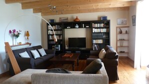 A living room with a sofa, a coffee table, a bookshelf, and a television. - Typical house, completely renovated, comfortable and warm. (Plonéour-Lanvern)