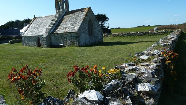 A stone church with a tall spire, surrounded by a stone wall and a grassy field. - Typical house, completely renovated, comfortable and warm. (Plonéour-Lanvern)