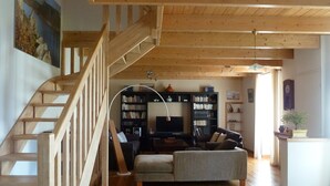 A spacious living area with a wooden staircase, a fireplace, and a large bookshelf. - Typical house, completely renovated, comfortable and warm. (Plonéour-Lanvern)