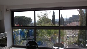 A kitchen with a large window overlooking a garden and a view of trees and buildings. - Cassis Large studio, Terrace, village and beach on foot, private parking in Provence (Cassis)