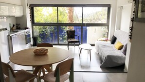 A modern kitchen with a dining area, a sofa, and a view of greenery through large windows. - Cassis Large studio, Terrace, village and beach on foot, private parking in Provence (Cassis)